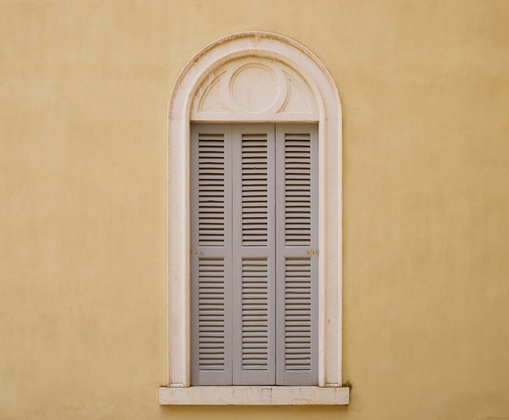 Fenster mit hölzernen Fensterläden auf gelber Wand