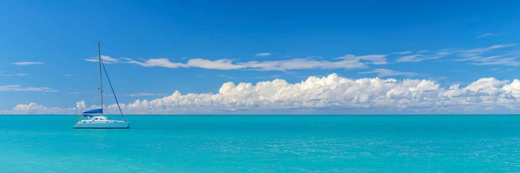 Panoramablick auf eine blaue Meereslandschaft mit Segelboot und bewölktem Himmel.