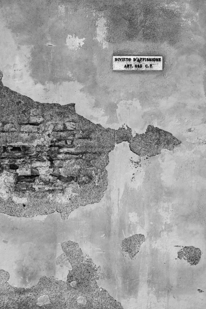 Verwitterte Mauer mit italienischem Text.