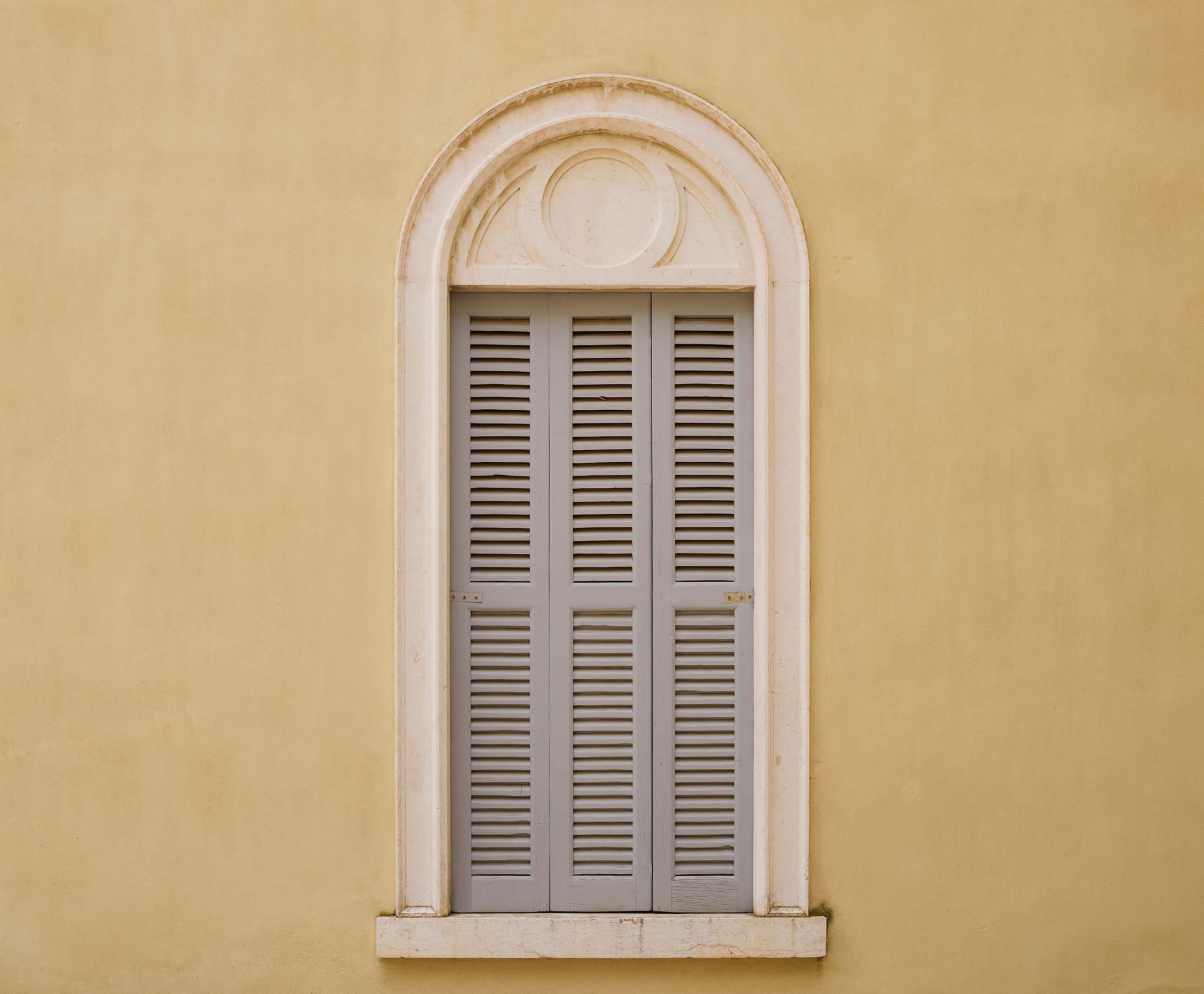 Fenster mit hölzernen Fensterläden auf gelber Wand