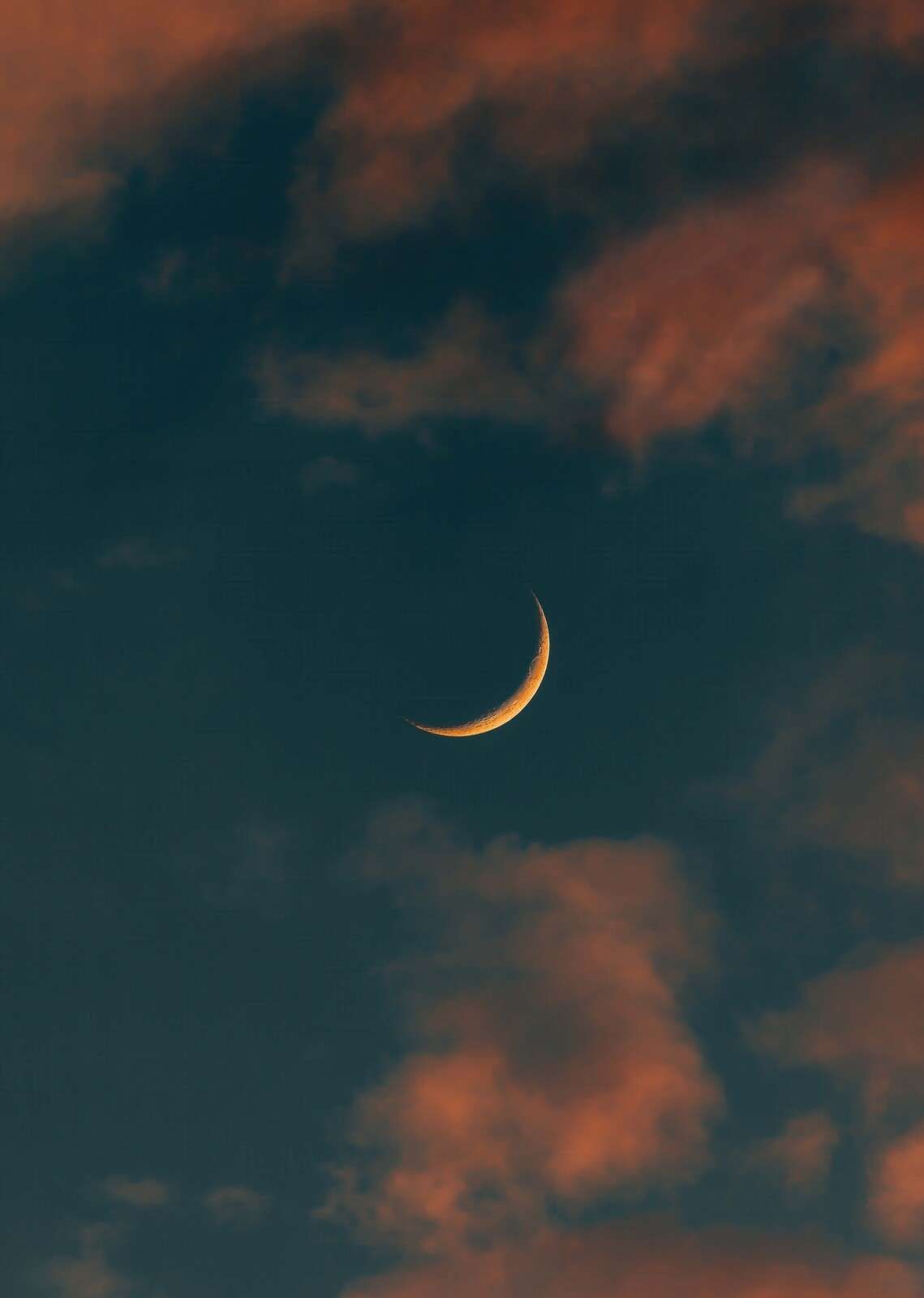 Schmale Mondsichel zwischen feurigen Wolken